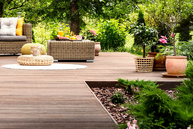 Beautiful wooden terrace with garden furniture surrounded by greenery on a warm, summer day