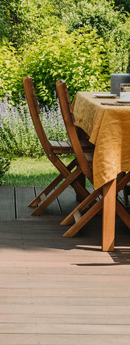 Dining table covered with orange tablecloth standing on wooden terrace in green garden